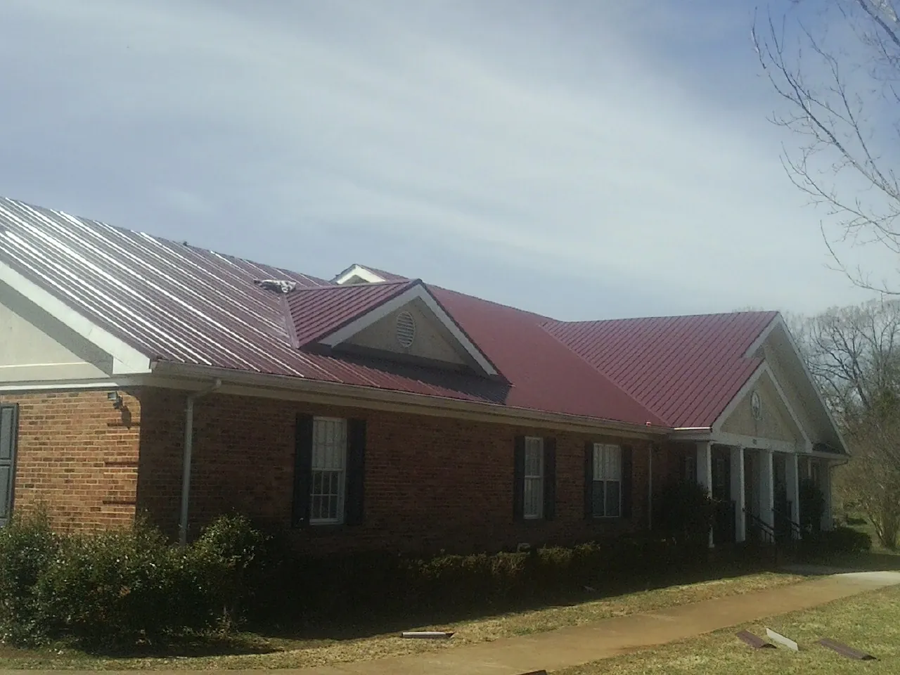 Red metal roof with gabled entries on a long brick building, from a Hail Damage Roof Repair job in Moshannon