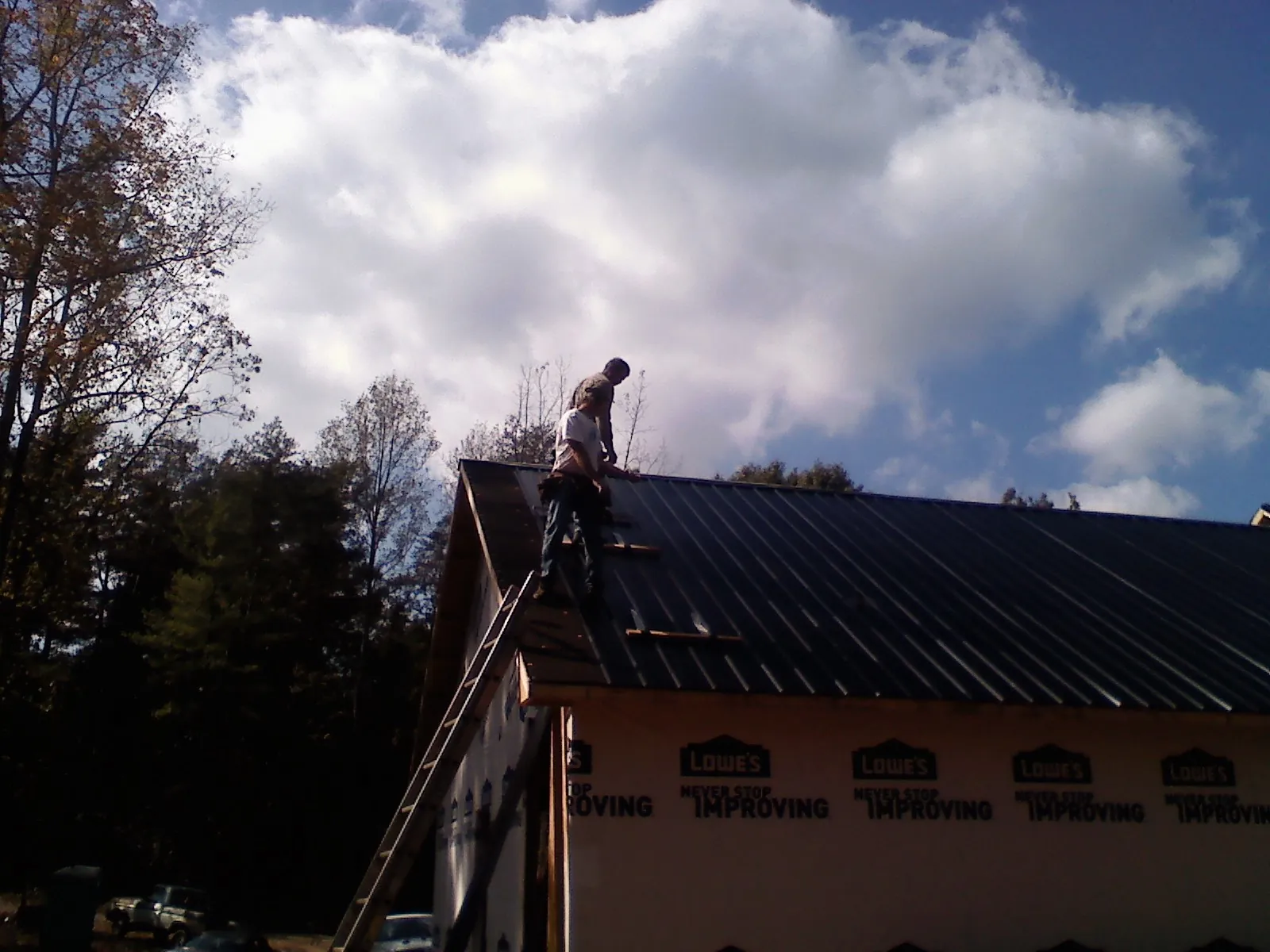 Roofer fastening dark metal panels high against a cloudy sky, from a Roof Inspection job in Moshannon