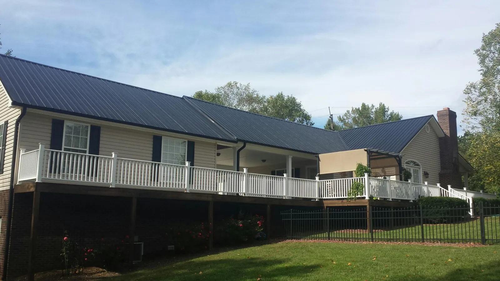 Black metal roof above a long white railed deck on a hillside home in Moshannon