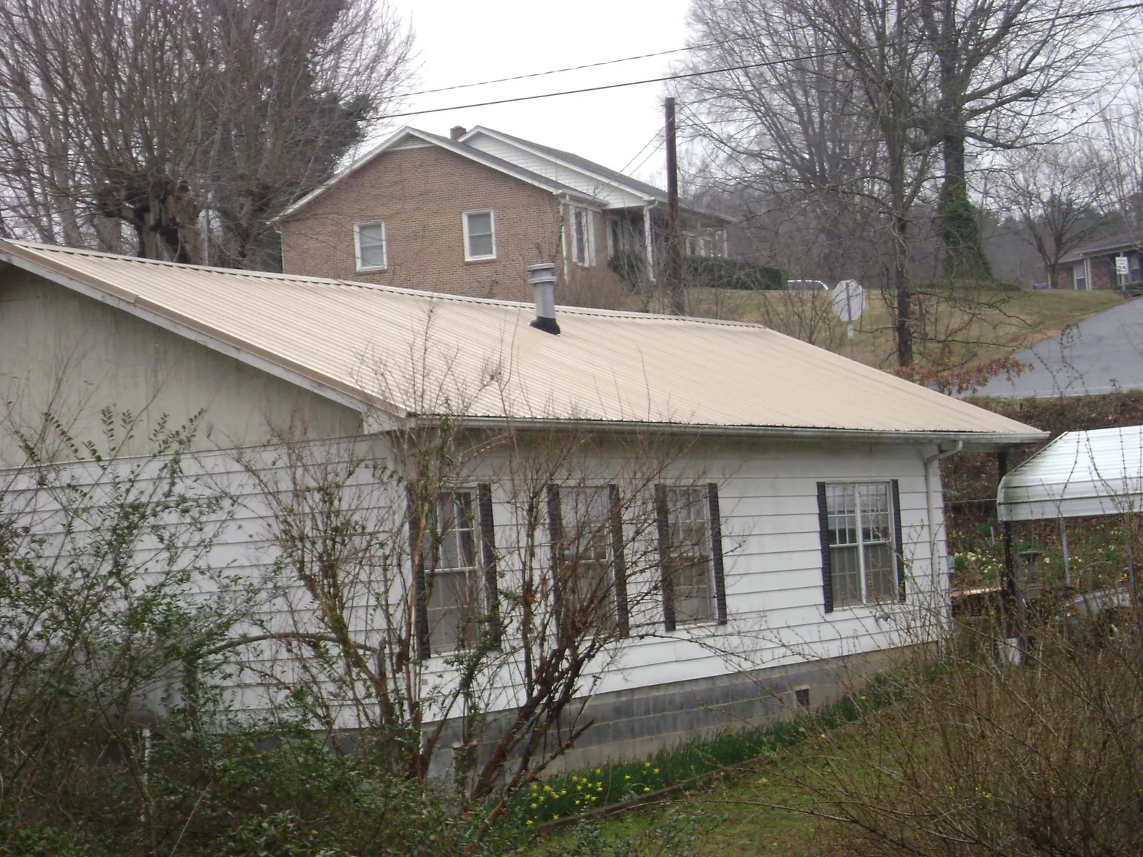 Tan metal roof on a white sided house set into a hillside — Commercial Roofing by Roofing Brothers in Moshannon