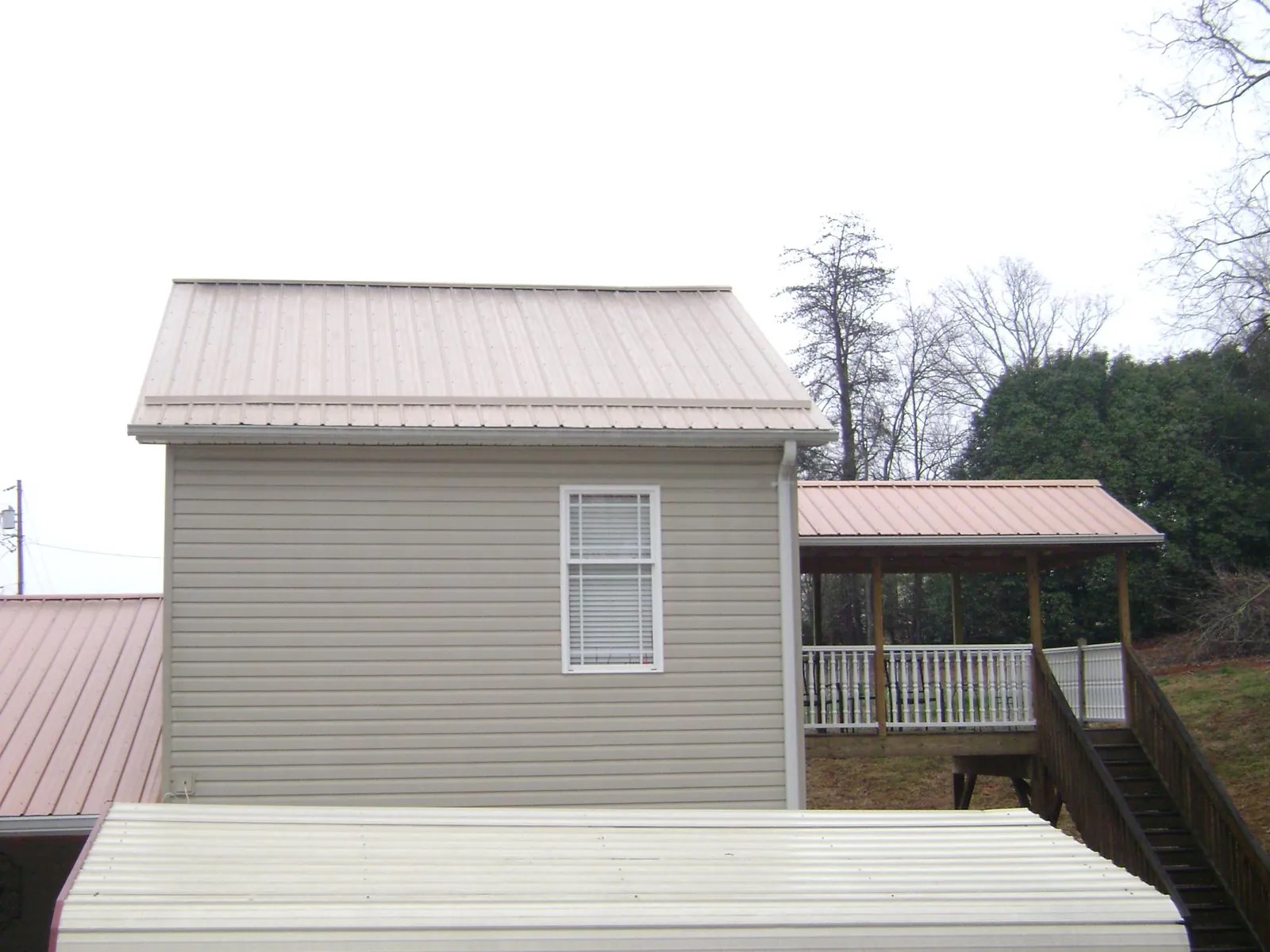 Tan metal roofs on a two story addition and attached porch, from a Roof Replacement job in Moshannon